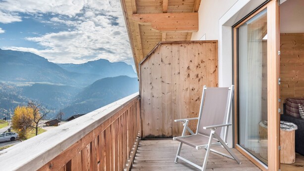A balcony with a wooden railing, a folding chair, and a sliding glass door leading to a room. - Holiday Apartment 'Hatzes App Raschötz' with Mountain View, Balcony and Wi-Fi (Lajen)
