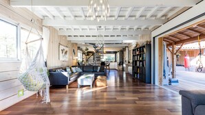 Uma sala de estar ampla, com piso de madeira, um sofá, uma mesa de centro e uma poltrona suspensa.