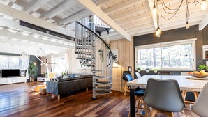 Uma sala de estar ampla com piso de madeira, escada, mesa de jantar com cadeiras e área de cozinha.