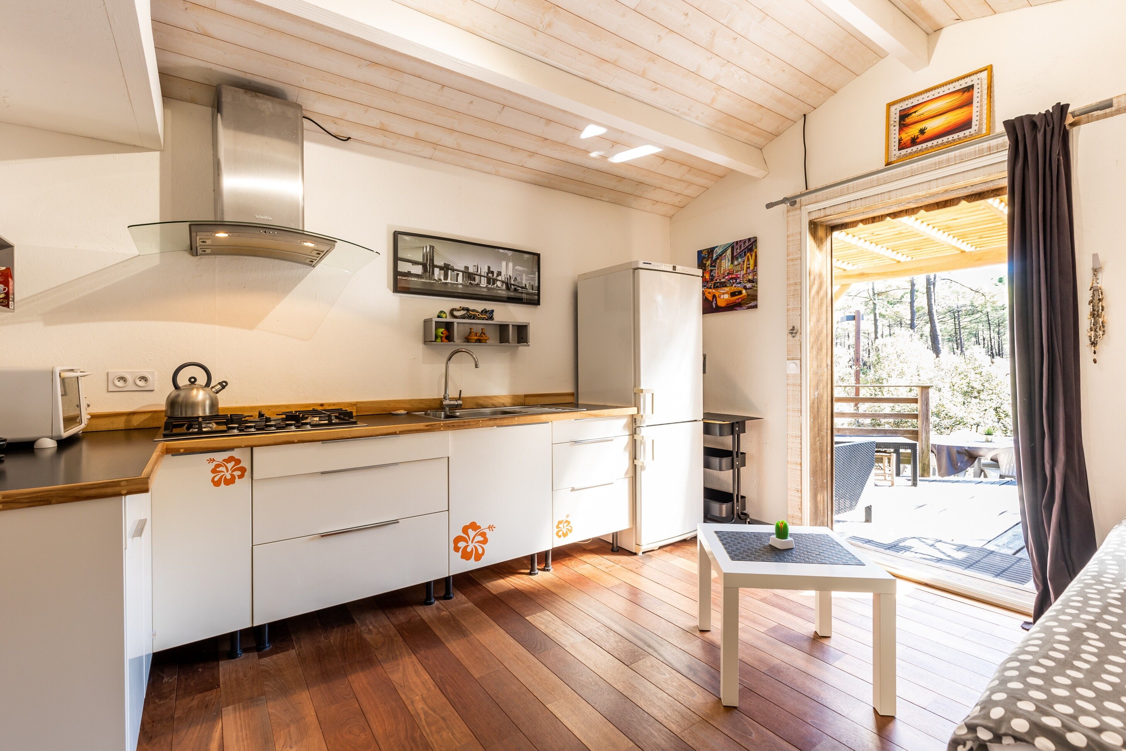 Une cuisine moderne avec un plancher en bois, une cuisinière à gaz, une hotte en acier inoxydable et un réfrigérateur.