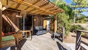 A wooden deck with outdoor furniture, a pergola, and a view of trees.