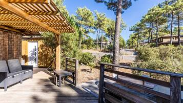 Une terrasse en bois avec un canapé et une table, entourée d’arbres et sous un ciel dégagé.