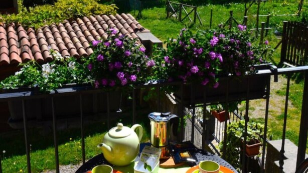 Una mesa con tetera, tazas y pasteles en un balcón con vista a la montaña.