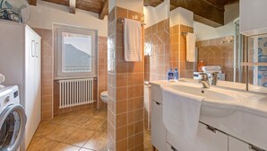 Ein Badezimmer mit Waschmaschine, Heizkörper, einem großen Fenster mit Bergblick und einem Waschbecken mit Handtuch.