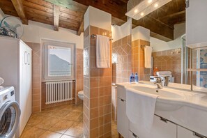 A bathroom with a washing machine, a radiator, a large window with a mountain view, and a sink with a towel.