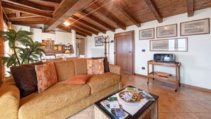 Ein Wohnzimmer mit Holzboden, einer Couch, einem Couchtisch mit Zeitschriften, einem Fernseher auf einem Schrank und einer Tür mit Kleiderhaken.