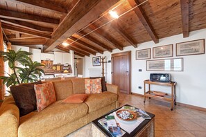 A living room with a wooden ceiling, a sofa, a coffee table with magazines, a television on a stand, and a door with a coat rack.