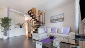 Een moderne woonkamer met een glazen salontafel, een witte bank en een trap met houten leuningen.