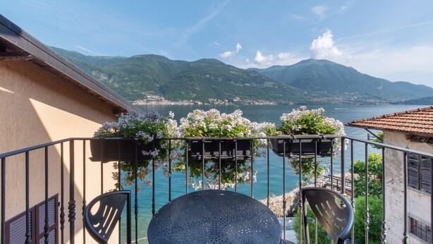 Een balkon met een tafel en stoelen, met uitzicht op een meer en bergen.