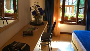 A room with a bed, a dining table with chairs, a window with curtains, and a vase with flowers.