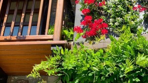 A wooden balcony with a stone wall, red flowers, and green foliage.