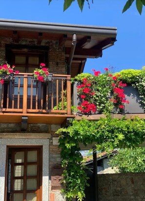 A building with a wooden balcony, a stone entrance, and flowering plants.