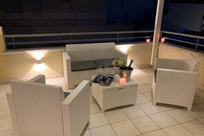 A balcony with wicker furniture, a table with glasses and a candle, and a view of the night sky.