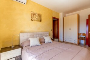 A bedroom with a bed, nightstand, bedside lamp, wardrobe, and a door.