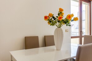 A dining table with a white vase containing yellow roses, brown chairs, and a window with a view of buildings.