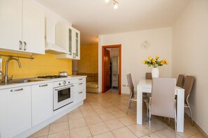 A modern kitchen with white cabinets, a stove, and a sink. There is a dining area with a table and chairs.