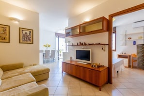 A modern living room with a sofa, TV, wooden cabinet, and a dining area with chairs and a table.