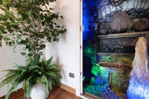 Une pièce avec une plante en pot, un mur décoratif à l’aspect pierre, et une étagère sur laquelle sont disposés divers objets.