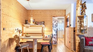 Ein gemütliches Zimmer mit Etagenbett, Holzwänden, einem Esstisch mit Stühlen, einer Couch und einem dekorativen Regal.