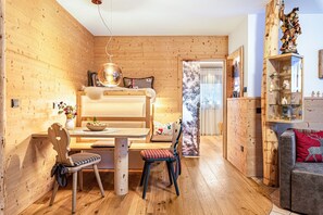 A cozy room with a bunk bed, wooden walls, a dining table with chairs, a sofa, and a decorative shelf.