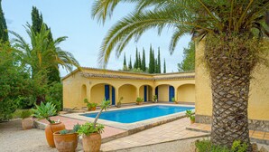 A pool with a tiled deck, a yellow building with blue doors, and potted plants. - Holiday Home 'Casa Babut' with Pool, Garden and Terrace (Pedreguer)
