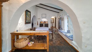 A narrow room with an arched ceiling, a wooden table with a checkered tablecloth, a bench with cushions, and a small altar with religious icons. - Holiday Home 'Casa Babut' with Pool, Garden and Terrace (Pedreguer)