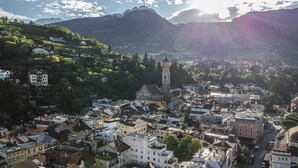 Eine Stadt mit einem markanten Kirchturm, umgeben von Wohnhäusern und einem Berg im Hintergrund.