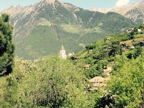 A mountainous landscape with a church and scattered houses. - Residence Hubertus Apartment 1 with Balcony & Wi-Fi (Meran)