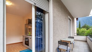 Ein Balkon mit Tisch und Stühlen, eine Schiebetür zu einer Küche und Blick auf Berge.