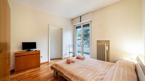 Ein Schlafzimmer mit einem Bett, einem Fernseher auf einer Holzkommode, einem Sessel und einem Fenster mit Blick.