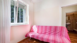 A room with a wooden herringbone floor, a pink-striped sofa, a window with white blinds, and a bathroom with a sink and mirror. - Residence Hubertus Apartment 5 with  Balcony & Wi-Fi (Meran)