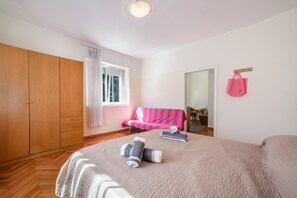 A bedroom with a bed, a wardrobe, a window with curtains, a pink sofa, and a pink bag on the wall.