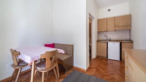 A compact kitchen with wooden cabinets, a white refrigerator, and a dining area with a bench and chairs. - Residence Hubertus Apartment 5 with  Balcony & Wi-Fi (Meran)