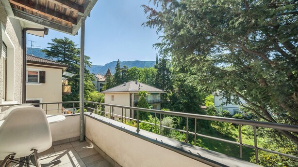 A balcony with a chair, a railing, and a view of houses and trees. - Residence Hubertus Apartment 5 with  Balcony & Wi-Fi (Meran)