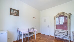 A room with a dining table, chairs, a white cabinet, a herringbone-patterned wooden floor, a door, and a vintage-style mirror. - Residence Hubertus Apartment 6 with Balcony & Wi-Fi (Meran)