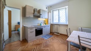 A compact kitchen with a herringbone floor, a dining table with chairs, and a window with curtains. - Residence Hubertus Apartment 6 with Balcony & Wi-Fi (Meran)