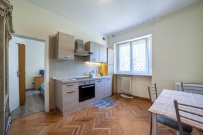A compact kitchen with a herringbone floor, a dining table with chairs, and a window with curtains.