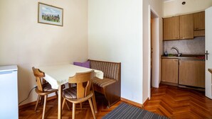 A compact kitchen with wooden cabinets, a dining table with chairs, a bench, and a small refrigerator. - Residence Hubertus Apartment 2 with Balcony & Wi-Fi (Meran)