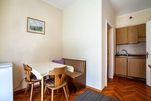 A compact kitchen with wooden cabinets, a dining table with chairs, a bench, and a small refrigerator.
