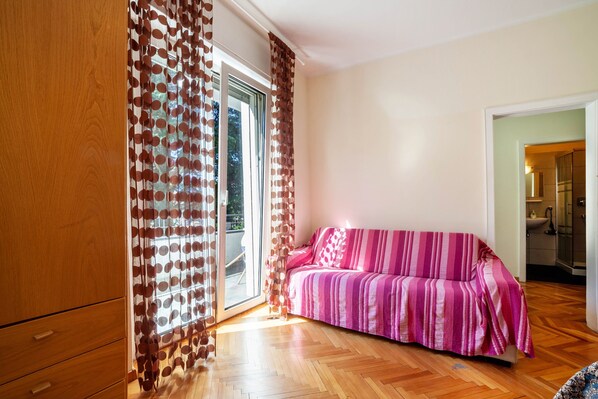 Une pièce avec un plancher en bois, un canapé à rayures roses et une porte-fenêtre coulissante agrémentée de rideaux à motifs.