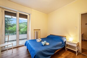 Una camera da letto con un letto, un comodino, una sedia, un termosifone e una porta scorrevole in vetro che dà su un balcone.