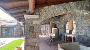 Une terrasse extérieure avec des murs en pierre, une cheminée en pierre et des meubles en osier.