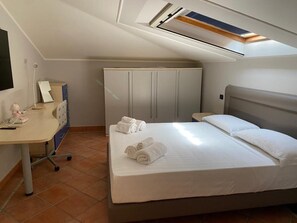 Une chambre à coucher avec un lit, un bureau, une armoire et une fenêtre de toit.