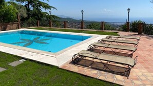 Une piscine rectangulaire ornée d’un motif décoratif, entourée d’une terrasse carrelée avec des chaises longues.