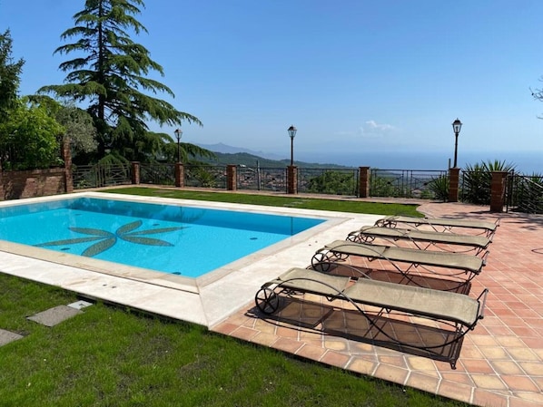 Une piscine rectangulaire ornée d’un motif décoratif, entourée d’une terrasse carrelée avec des chaises longues.