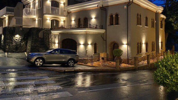 Une grande maison à étages, dotée d’une façade en pierre, d’un balcon et d’une voiture garée devant.