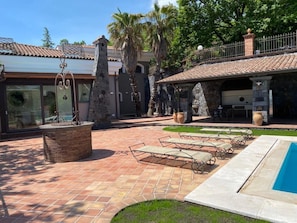 Zona de piscina con sillones de descanso, una fuente de piedra y un patio con pérgola.