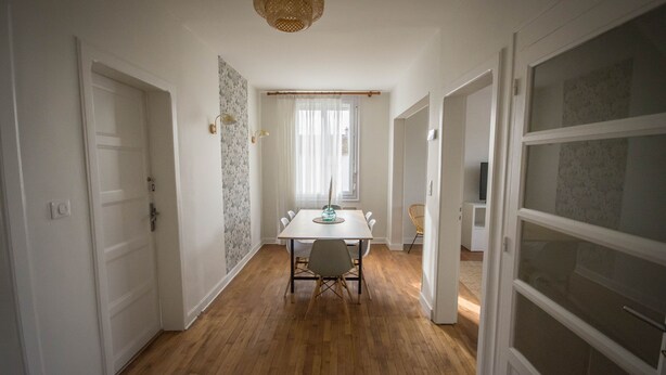 A spacious room with a wooden floor, a dining table with chairs, a hanging light fixture, and a large window with sheer curtains. - Large 220m2 house, near town center with garden (Limoges)