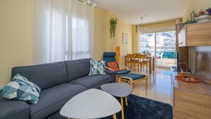 Een moderne woonkamer met een bank, twee bijzettafels, een eethoek met stoelen en uitzicht op buiten.