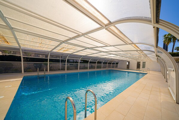 A swimming pool with a glass ceiling, metal railings, and a tiled floor.